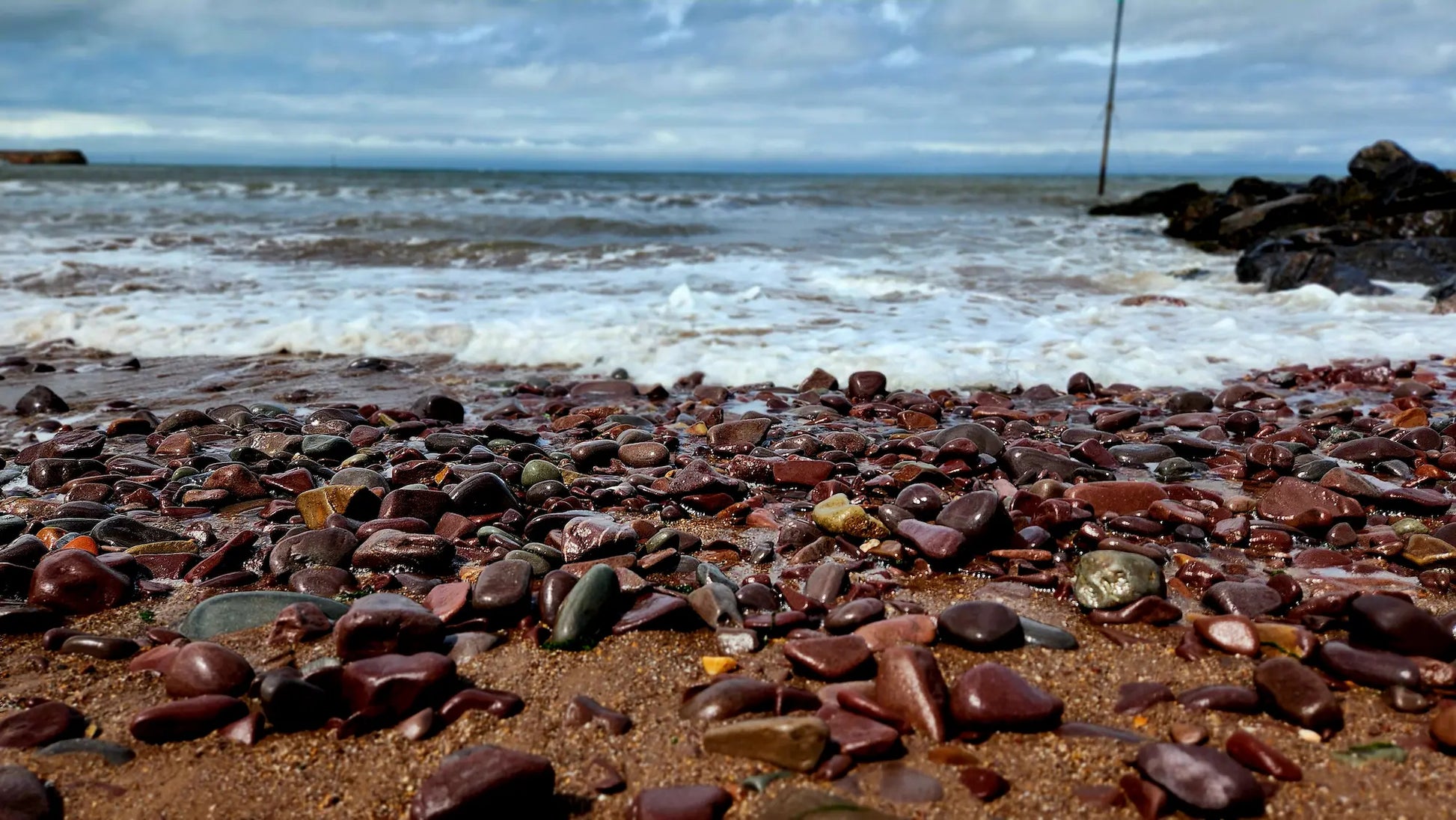Stones on Minehead beach with ocean waves and sky in the background