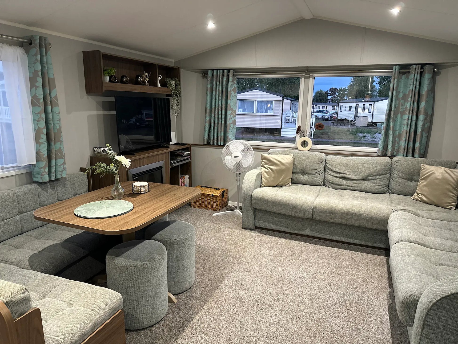 Butlins Caravan Living room with grey sofa, wooden table, 43 inch 4K TV and curtains.