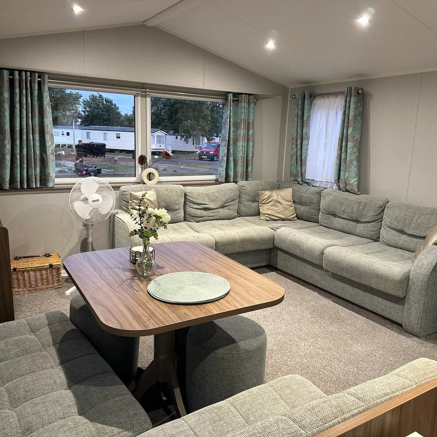 Butlins Caravan Living room with a sectional sofa, wooden table, and decorative items.