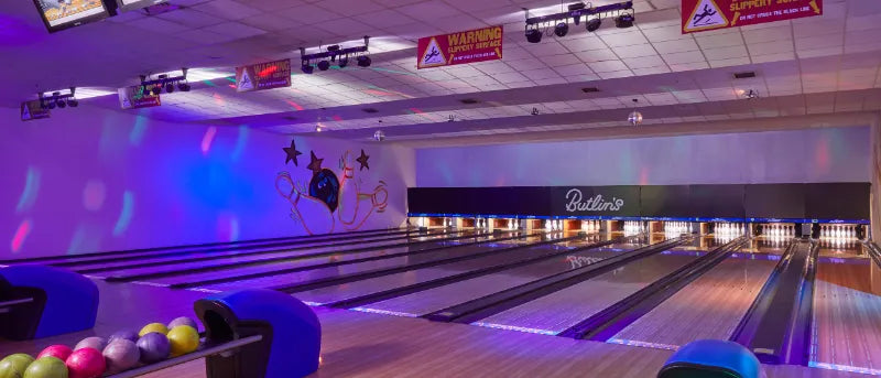 Bowling alley with lanes and pins, illuminated by purple and blue lights.