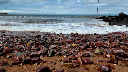 Stones on Minehead beach with ocean waves and sky in the background