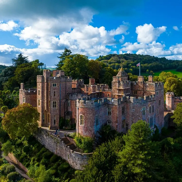 Dunster castle surrounded by green trees under a blue sky with white clouds