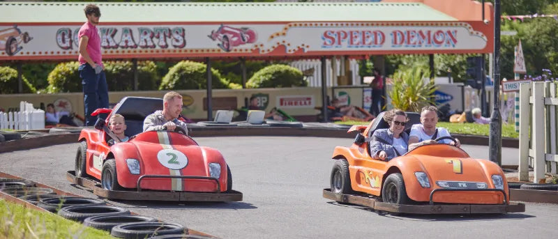 People driving go-karts at a speed demon track with a sign in the background.