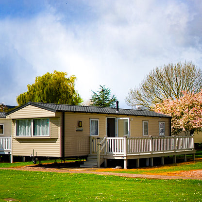 Caravan with a decked veranda in a park setting with trees and grass.