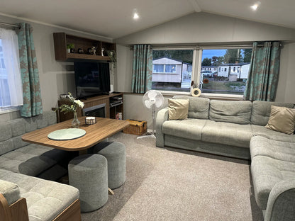 Butlins Caravan Living room with grey sofa, wooden table, 43 inch 4K TV and curtains.