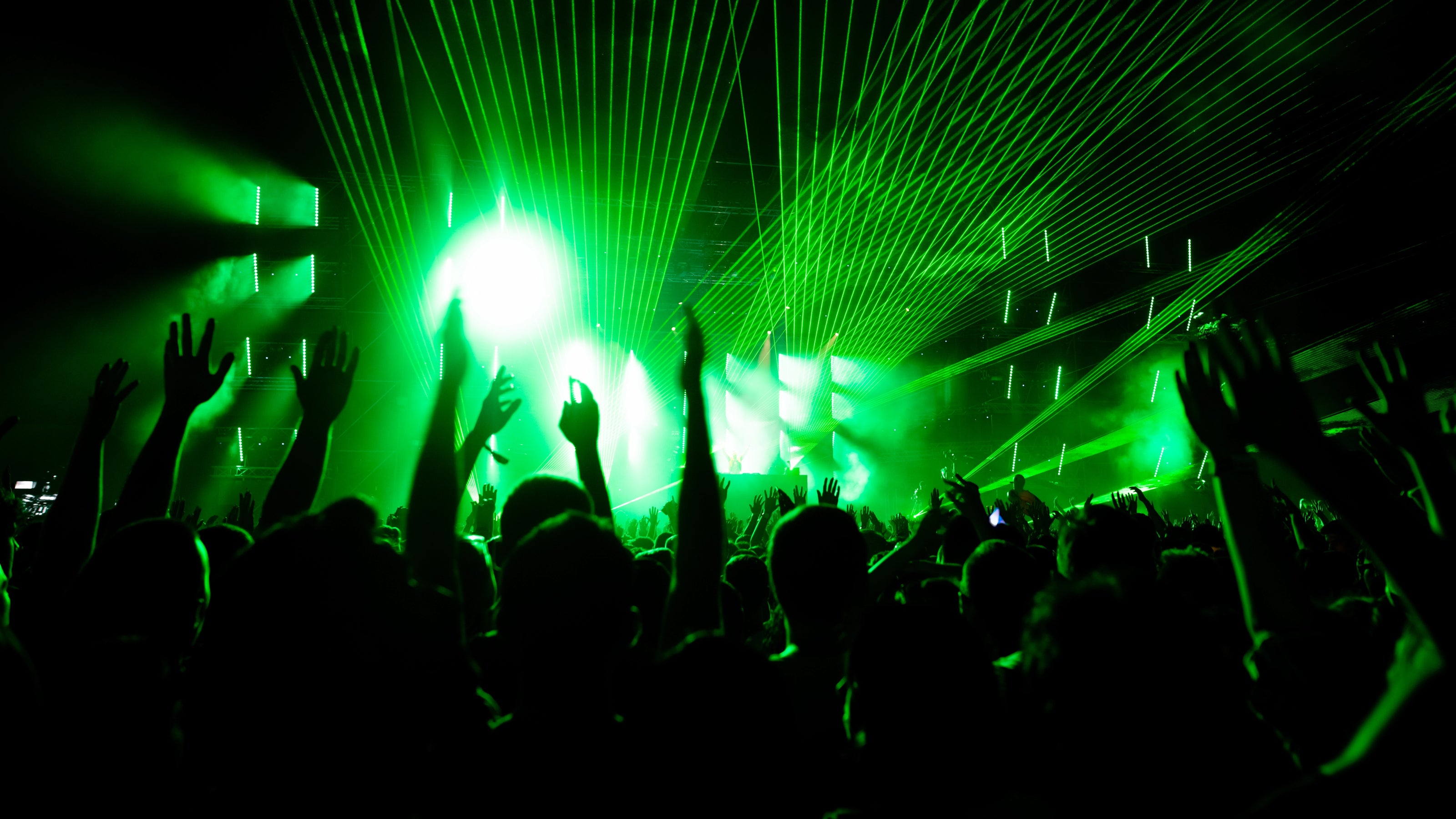 People at a Butlin's Adult weekender concert with green laser lights and stage lights.