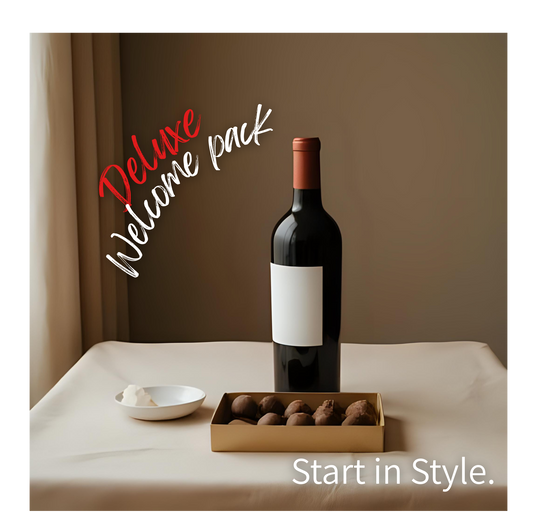 Bottle of wine with a box of chocolates and a bowl on a table, labeled 'Deluxe Welcome Pack'.