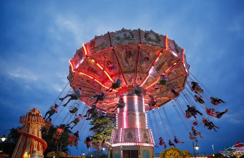 Amusement park ride with people on swings at night under a blue sky.
